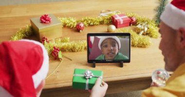 Noel Baba şapkalı beyaz bir baba ve oğul, ekrandaki çocukla noel videosu için tablet kullanıyorlar. Noel, şenlik ve iletişim teknolojisi.
