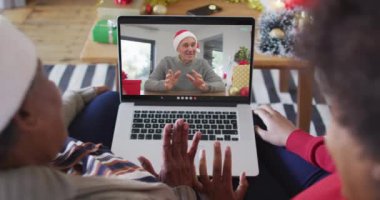 Afrika kökenli Amerikalı anne ve kız. Ekrandaki adamla yılbaşı videosu için dizüstü bilgisayar kullanıyorlar. Noel, şenlik ve iletişim teknolojisi.