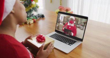 Noel Baba şapkalı Afrikalı bir kadın Noel Baba 'nın ekranında dizüstü bilgisayar kullanıyor. Covid 19 salgını sırasında Noel, şenlik ve iletişim teknolojisi.