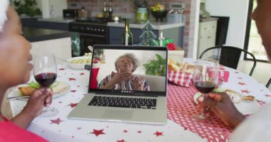 Şaraplı gülümseyen Afro-Amerikan çift ekranda kadınla Noel görüntülü konuşma için dizüstü bilgisayar kullanıyor. Noel, şenlik ve iletişim teknolojisi.