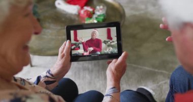 Üst düzey Kafkasyalı çift, ekranda gülümseyen adamla noel videosu için tablet kullanıyor. Noel, şenlik ve iletişim teknolojisi.