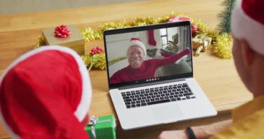 Noel Baba şapkalı beyaz bir baba ve oğul, ekrandaki adamla yılbaşı görüntülerinde dizüstü bilgisayar kullanıyorlar. Noel, şenlik ve iletişim teknolojisi.