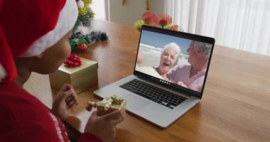 Noel Baba şapkalı Afro-Amerikalı bir kadın Noel 'de ekranda çift olarak dizüstü bilgisayar kullanıyor. Noel, şenlik ve iletişim teknolojisi.