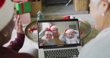 İki farklı kıdemli bayan arkadaş, ekranda ailesiyle birlikte yılbaşı videosu için dizüstü bilgisayar kullanıyor. Noel, şenlik ve iletişim teknolojisi.