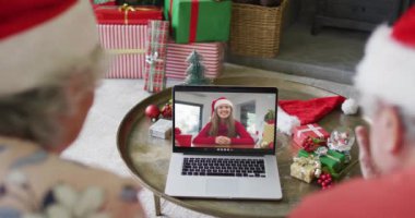 Üst düzey Kafkasyalı çift, ekranda gülümseyen bir kadınla yılbaşı görüntüsü için dizüstü bilgisayar kullanıyor. Noel, şenlik ve iletişim teknolojisi.