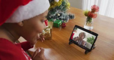 Noel Baba şapkalı Afrikalı Amerikalı bir kadın Noel için tablet kullanıyor ve ekranda bir kadın var. Noel, şenlik ve iletişim teknolojisi.