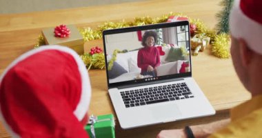 Noel Baba şapkalı beyaz bir baba ve oğul, ekranda bir kadınla yılbaşı görüntüsü için dizüstü bilgisayar kullanıyorlar. Noel, şenlik ve iletişim teknolojisi.