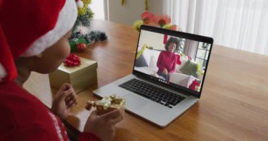 Noel Baba şapkalı Afro-Amerikalı bir kadın Noel 'de ekranda arkadaşıyla birlikte laptop kullanıyor. Noel, şenlik ve iletişim teknolojisi.