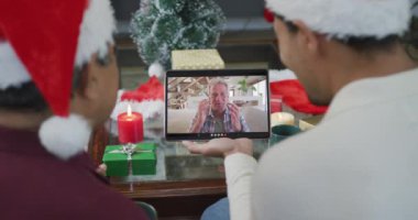 Oğlu el sallayan melez bir baba ve ekranda bir adamla noel videosu için tablet kullanıyor. Noel, şenlik ve iletişim teknolojisi.
