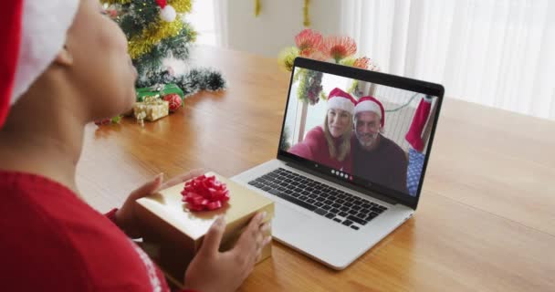 クリスマスのビデオ通話のためにラップトップを使用してサンタの帽子を持つアフリカ系アメリカ人の女性 画面上のカップル クリスマスやお祭りや通信技術は — ストック動画