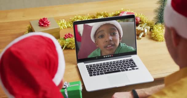 白人父亲带着头戴圣诞帽的儿子用笔记本电脑打圣诞视频 男孩出现在屏幕上 圣诞节 节日和通信技术 — 图库视频影像