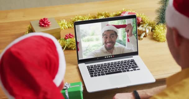 クリスマスのビデオ通話のためのラップトップを使用してサンタの帽子を持つ息子と白人の父 画面上の男と クリスマスやお祭りや通信技術は — ストック動画