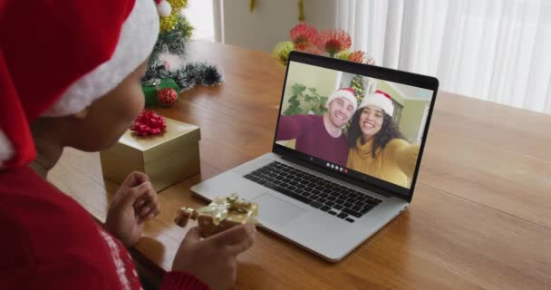 クリスマスのビデオ通話のためにラップトップを使用してサンタの帽子を持つアフリカ系アメリカ人の女性 画面上のカップル クリスマスやお祭りや通信技術は — ストック動画
