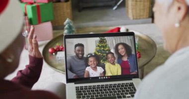 İki farklı kıdemli bayan arkadaş, ekranda ailesiyle birlikte yılbaşı videosu için dizüstü bilgisayar kullanıyor. Noel, şenlik ve iletişim teknolojisi.