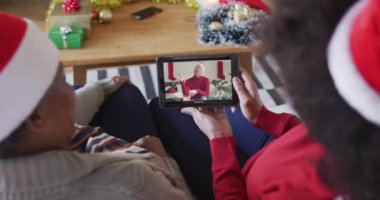 Afrika kökenli Amerikalı anne ve kız. Ekranda bir adamla noel videosu için tablet kullanıyorlar. Noel, şenlik ve iletişim teknolojisi.