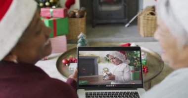 İki farklı kıdemli bayan arkadaş, ekrandaki çocukla yılbaşı videosu için dizüstü bilgisayar kullanıyor. Noel, şenlik ve iletişim teknolojisi.