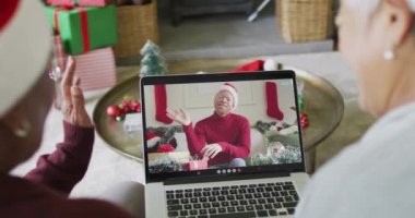 Ekrandaki adamla yılbaşı görüntülü görüşmesi için dizüstü bilgisayar kullanan iki farklı son sınıf kız arkadaş. Noel, şenlik ve iletişim teknolojisi.