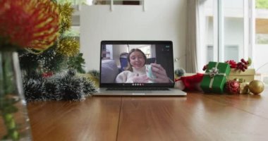 Gülümseyen Kafkasyalı kadın, dizüstü bilgisayardan yılbaşı videosunda kahve içiyor. Noel, şenlik ve iletişim teknolojisi.