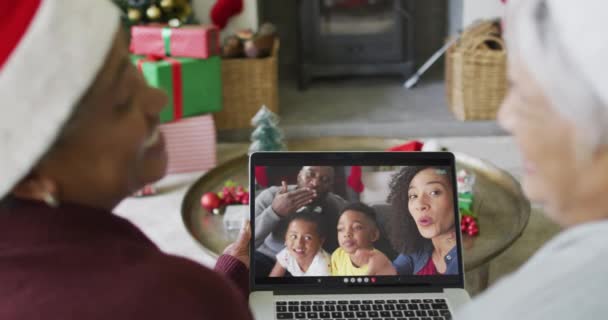 スクリーン上の家族とクリスマスのビデオ通話のためのラップトップを使用して2つの多様なシニア女性の友人 クリスマスやお祭りや通信技術は — ストック動画