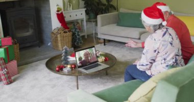Noel Baba şapkalı son sınıf Kafkasyalı çift ekrandaki adamla yılbaşı görüntüsü için laptop kullanıyor. Noel, şenlik ve iletişim teknolojisi.