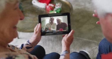 Gülümseyen Kafkasyalı çift, ekranda ailesiyle birlikte Noel için tablet kullanıyor. Noel, şenlik ve iletişim teknolojisi.