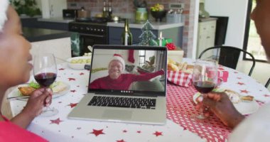 Şaraplı Afrika kökenli Amerikalı bir çift, ekrandaki adamla yılbaşı görüntüsü için laptop kullanıyor. Noel, şenlik ve iletişim teknolojisi.