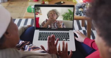 Afrika kökenli Amerikalı anne ve kız. Ekrandaki kadınla yılbaşı videosu için dizüstü bilgisayar kullanıyorlar. Noel, şenlik ve iletişim teknolojisi.