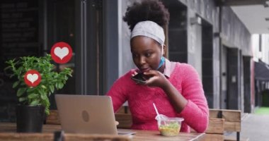 Kafede dizüstü bilgisayarı ve akıllı telefonu olan Afro-Amerikan bir kadının sosyal medya kalp ikonlarının canlandırılması. küresel iletişim teknolojisi ve sosyal ağ konsepti dijital olarak oluşturulmuş video.