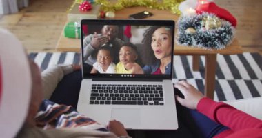 Afrika kökenli Amerikalı anne ve kız, ekranda ailesiyle birlikte yılbaşı görüntülü konuşma için dizüstü bilgisayar kullanıyorlar. Noel, şenlik ve iletişim teknolojisi.