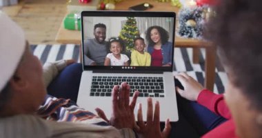 Afrika kökenli Amerikalı anne ve kız, ekranda ailesiyle birlikte yılbaşı görüntülü konuşma için dizüstü bilgisayar kullanıyorlar. Noel, şenlik ve iletişim teknolojisi.