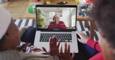 Afrika kökenli Amerikalı anne ve kız. Ekrandaki kadınla yılbaşı videosu için dizüstü bilgisayar kullanıyorlar. Noel, şenlik ve iletişim teknolojisi.