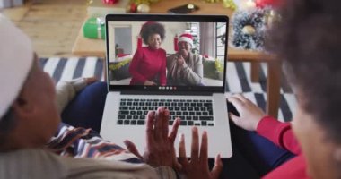 Afrika kökenli Amerikalı anne ve kız, ekranda ailesiyle birlikte yılbaşı görüntülü konuşma için dizüstü bilgisayar kullanıyorlar. Noel, şenlik ve iletişim teknolojisi.