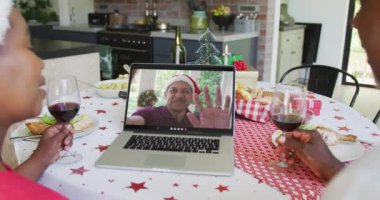 Şaraplı Afrika kökenli Amerikalı bir çift, ekrandaki adamla yılbaşı görüntüsü için laptop kullanıyor. Noel, şenlik ve iletişim teknolojisi.