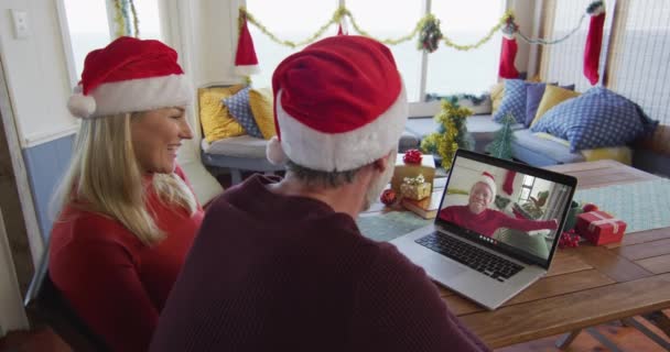 用笔记本电脑和男人一起在屏幕上进行圣诞视频通话 笑着带着桑塔帽的高加索夫妇 圣诞节 节日和通信技术 — 图库视频影像