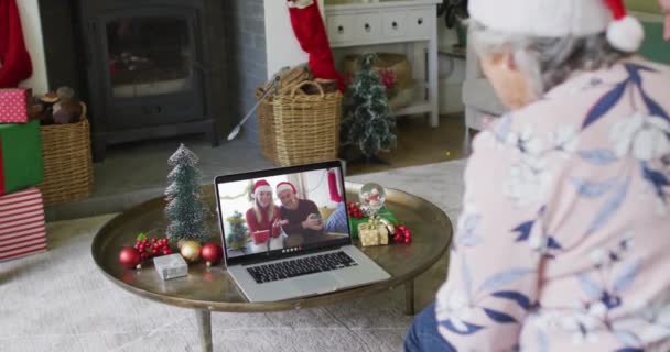 年长的高加索女人一边挥手一边用笔记本电脑给屏幕上有夫妻的圣诞视频打电话 圣诞节 节日和通信技术 — 图库视频影像