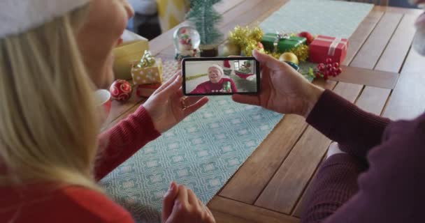 白种人夫妇与桑塔帽使用智能手机与男人在屏幕上的圣诞视频通话 圣诞节 节日和通信技术 — 图库视频影像