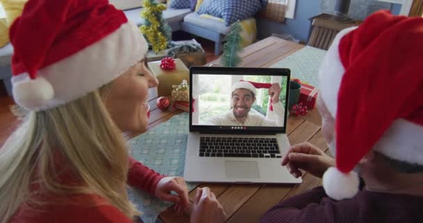 用笔记本电脑和男人一起在屏幕上进行圣诞视频通话 笑着带着桑塔帽的高加索夫妇 圣诞节 节日和通信技术 — 图库视频影像