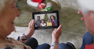 Gülümseyen Kafkasyalı son sınıf çifti, ekranda ailesiyle birlikte noel videosu için tablet kullanıyor. Noel, şenlik ve iletişim teknolojisi.