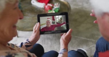 Gülümseyen Kafkasyalı son sınıf çifti, ekrandaki adamla noel videosu için tablet kullanıyor. Noel, şenlik ve iletişim teknolojisi.