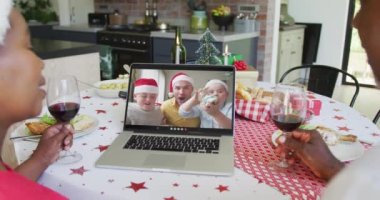 Şaraplı Afro-Amerikalı çift, dizüstü bilgisayarlarını ekranda aileleri ile birlikte yılbaşı görüntüsü için kullanıyorlar. Noel, şenlik ve iletişim teknolojisi.