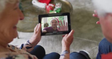 Gülümseyen Kafkasyalı çift, ekranda bir adamla noel videosu için tablet kullanıyor. Noel, şenlik ve iletişim teknolojisi.