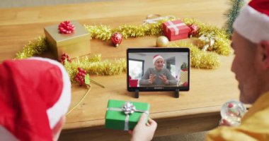 Noel Baba şapkalı beyaz bir baba ve oğul, ekranda bir adamla noel videosu için tablet kullanıyorlar. Noel, şenlik ve iletişim teknolojisi.