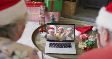 Noel Baba şapkalı son sınıf Kafkasyalı çift ekranda aileleriyle birlikte Noel 'de bilgisayar kullanıyorlar. Noel, şenlik ve iletişim teknolojisi.