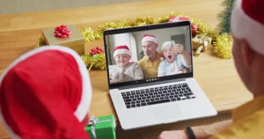 Noel Baba şapkalı beyaz bir baba ve oğul, ekranda aileleriyle yılbaşı görüntülerinde dizüstü bilgisayar kullanıyorlar. Noel, şenlik ve iletişim teknolojisi.