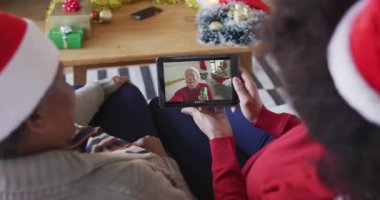 Afrika kökenli Amerikalı anne ve kız. Ekranda bir adamla noel videosu için tablet kullanıyorlar. Noel, şenlik ve iletişim teknolojisi.