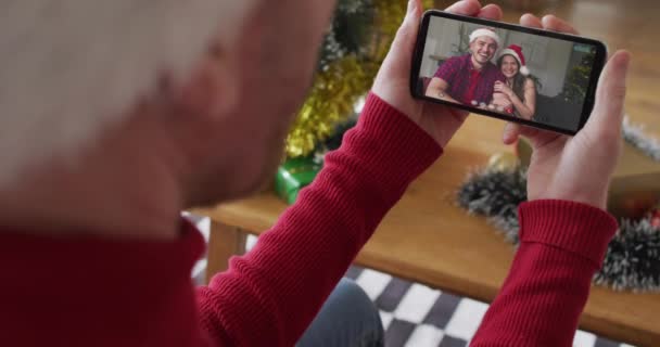 画面上の笑みを浮かべてカップルとクリスマスのビデオ通話のためのスマートフォンを使用してサンタの帽子を持つ白人男性 クリスマスやお祭りや通信技術は — ストック動画