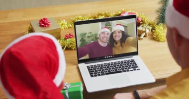 Noel Baba şapkalı beyaz bir baba ve oğul. Ekranda bir çiftle yılbaşı görüntüsü için dizüstü bilgisayar kullanıyorlar. Noel, şenlik ve iletişim teknolojisi.