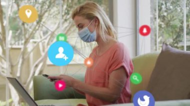 Evdeki akıllı telefonu kullanarak beyaz maskeli beyaz kadın üzerindeki dijital simgelerin canlandırılması. covid 19 pandemik konsept sırasında dijital olarak oluşturulan iletişim ve sosyal medya.