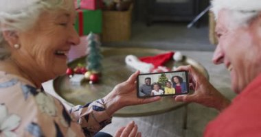 Gülümseyen Kafkasyalı son sınıf çifti ekranda ailesiyle yılbaşı videosu için akıllı telefon kullanıyor. Noel, şenlik ve iletişim teknolojisi.