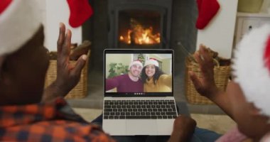 Noel Baba şapkalı Afro-Amerikan çift, dizüstü bilgisayarlarını ekranda çift olarak Noel 'de görüntülü konuşma için kullanıyorlar. Noel, şenlik ve iletişim teknolojisi.